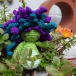 Medusa amigurumi de cabello turquesa frente a flores